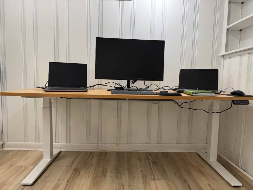 Electric standing desk setup in a home office with large monitor and ergonomic workspace